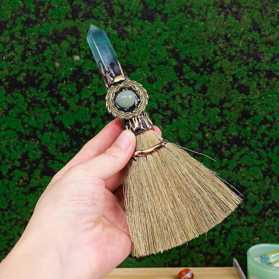 Hand holding a broom with a crystal handle against a green background