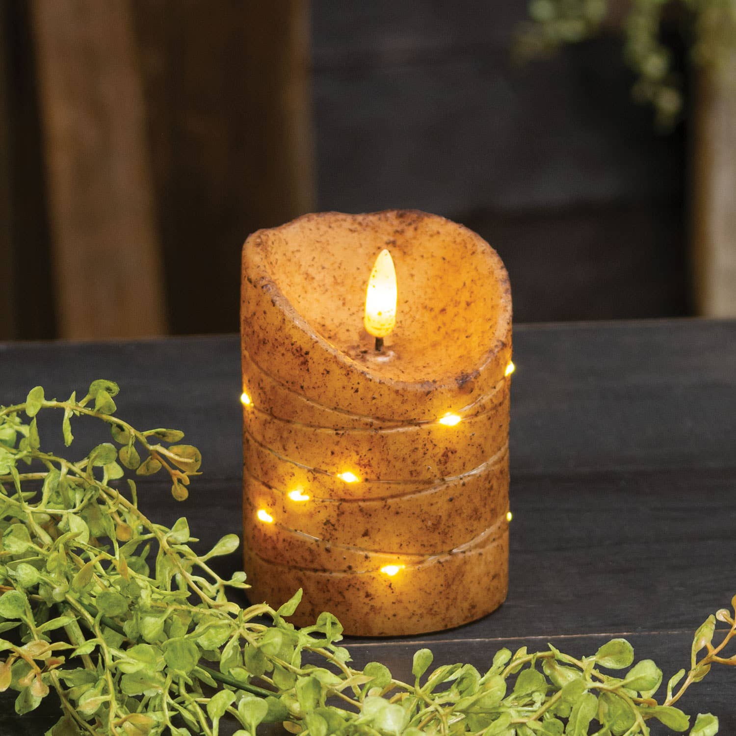 Decorative candle with LED lights on a dark surface with greenery