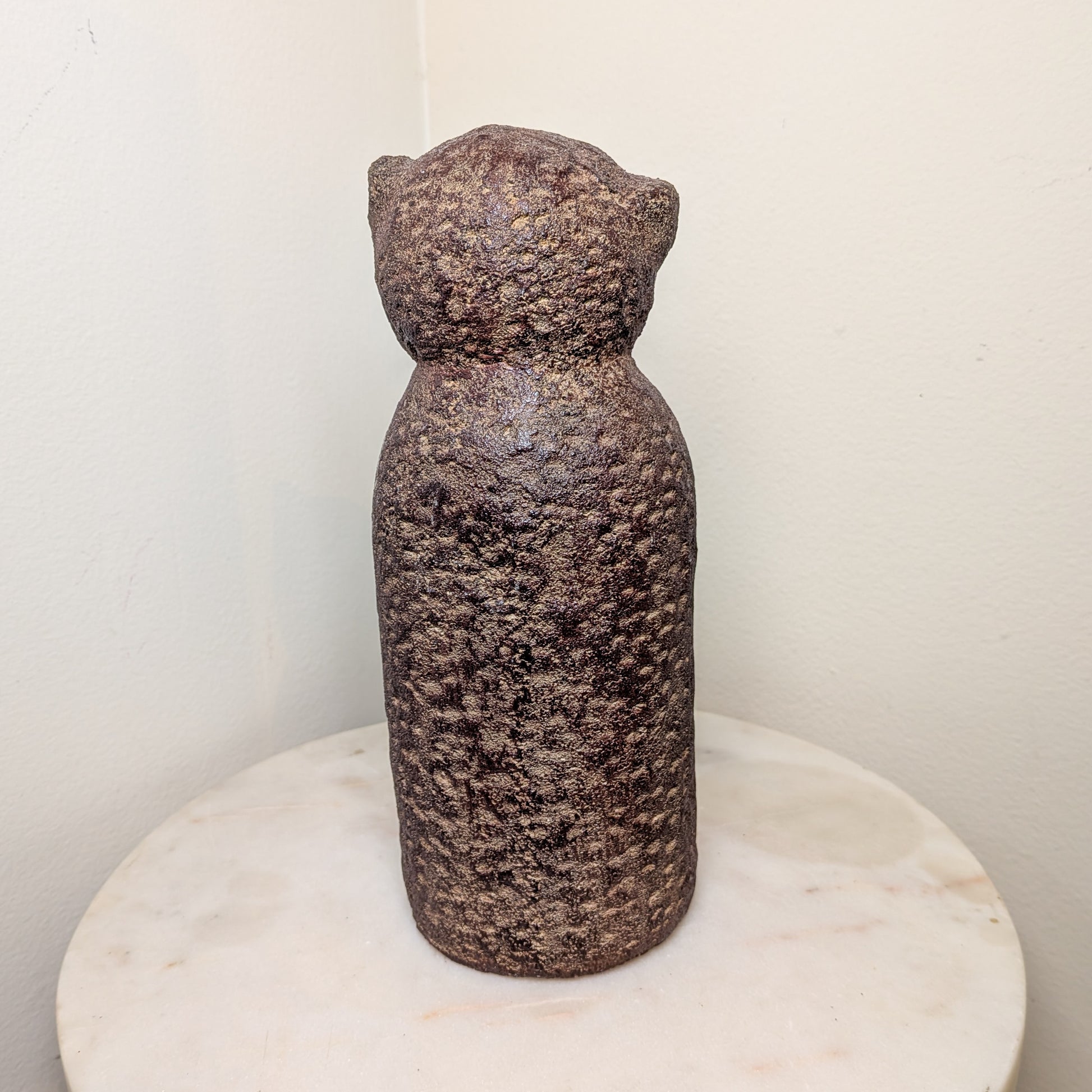 Textured stone sculpture on a marble base against a plain background
