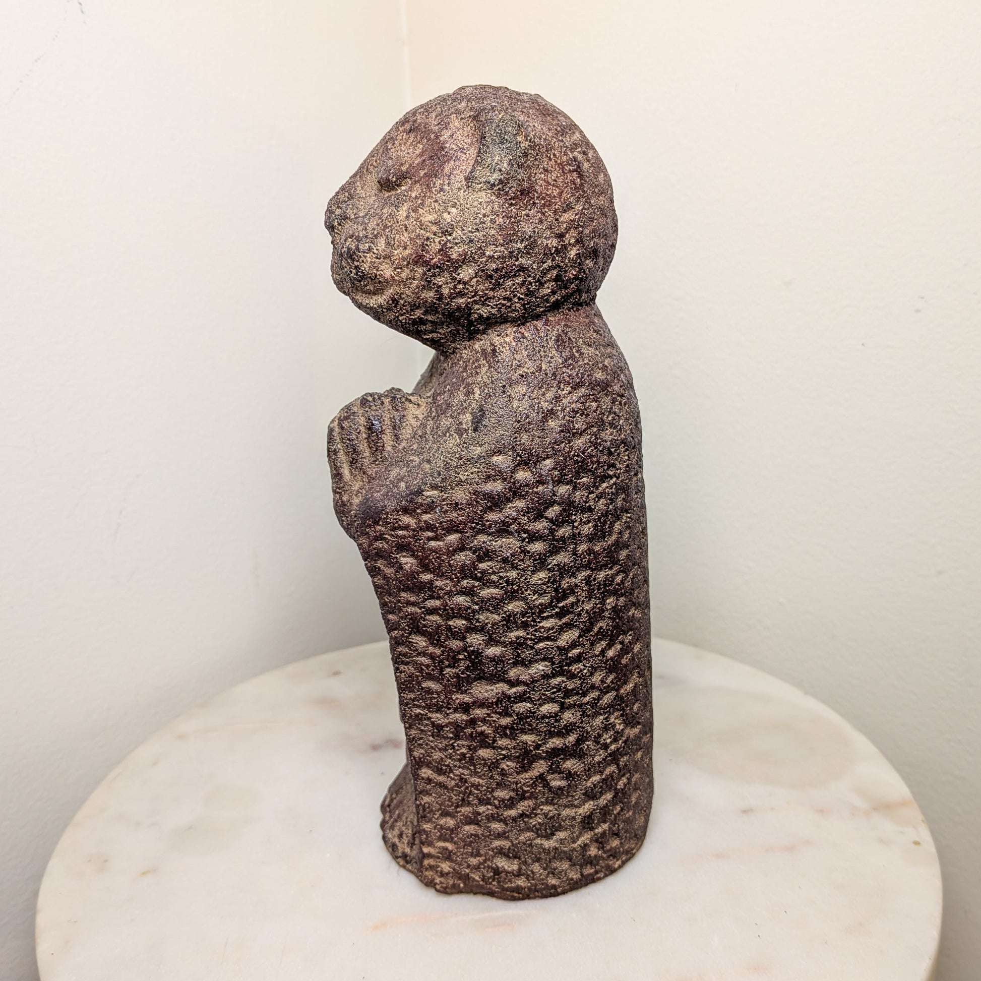 Stylized stone sculpture of a figure on a white pedestal against a plain background