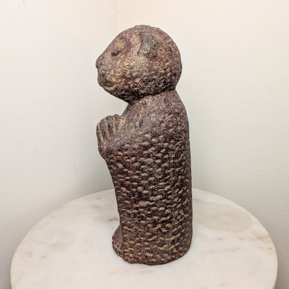 Stylized stone sculpture of a figure on a white pedestal against a plain background