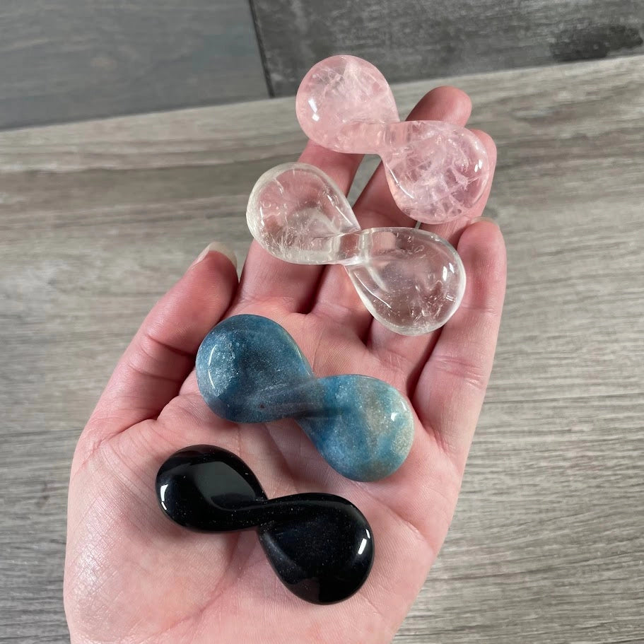 Carved crystal infinity symbols in obsidian, clear quartz, rose quartz, and trolleite