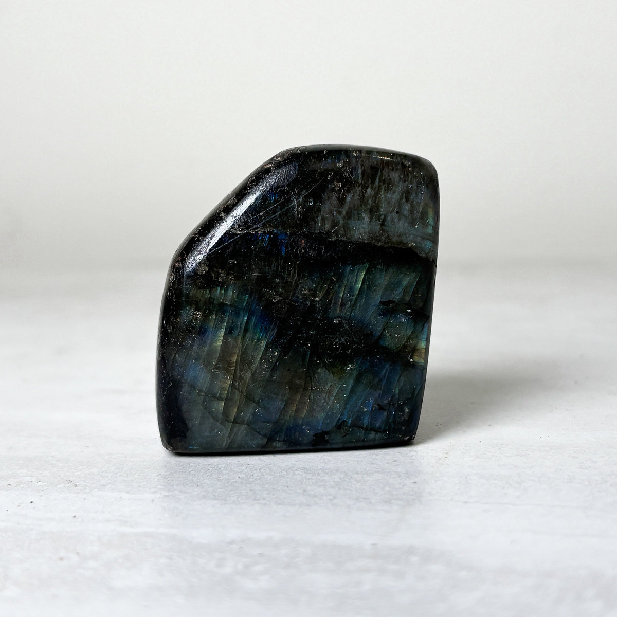 Small angular labradorite freeform with a flat top edge, showing muted green and gold flash across the dark polished surface.