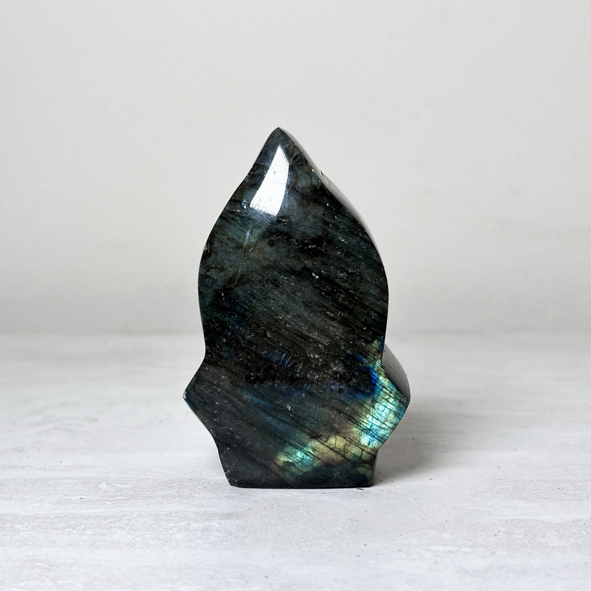 arrow head shaped labradorite freeform carved to a point, dark gray-green stone with teal and gold flash along the lower half.