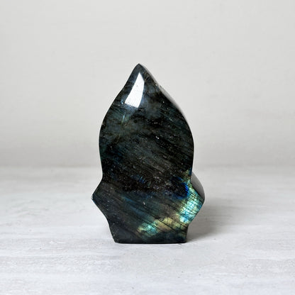 arrow head shaped labradorite freeform carved to a point, dark gray-green stone with teal and gold flash along the lower half.
