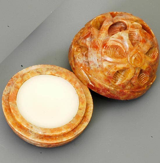 A hand-carved stone jar with its lid beside it, containing natural solid lily of the valley perfume.