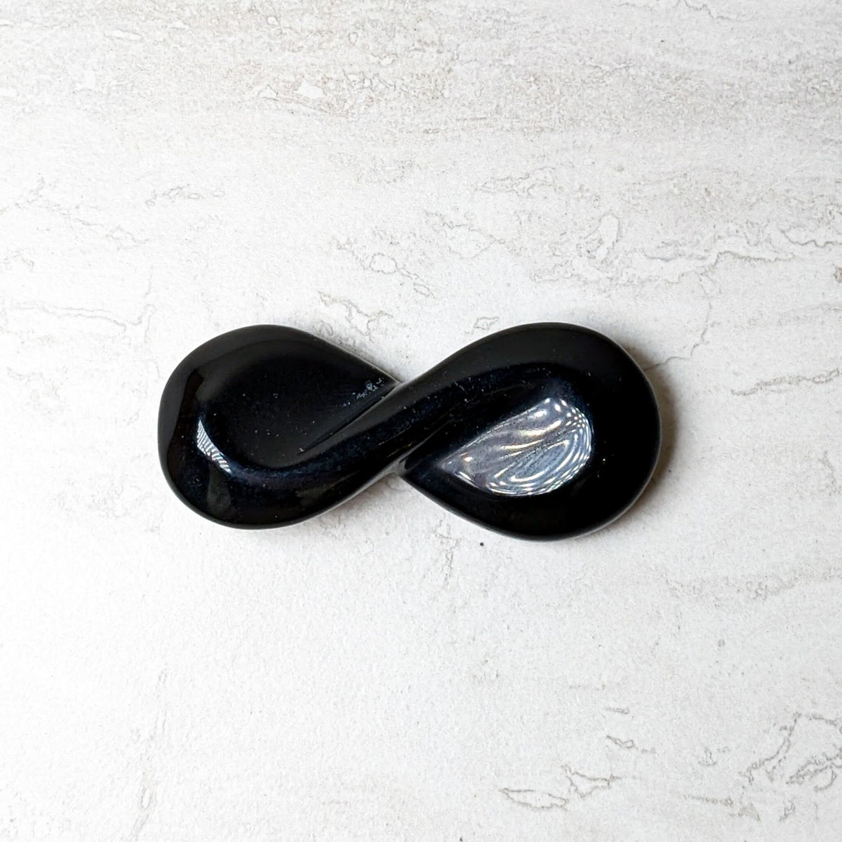 Black obsidian carved infinity symbol with a polished glossy finish